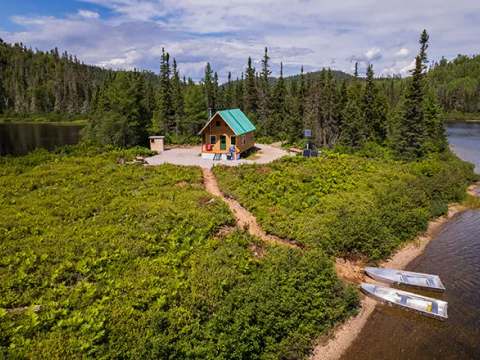 Vue aérienne du chalet numéro trois situé en bordure de lac, entouré d'une forêt dense.