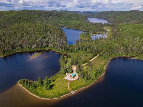 Vue aérienne du chalet situé en bordure du lac, entouré par la forêt.