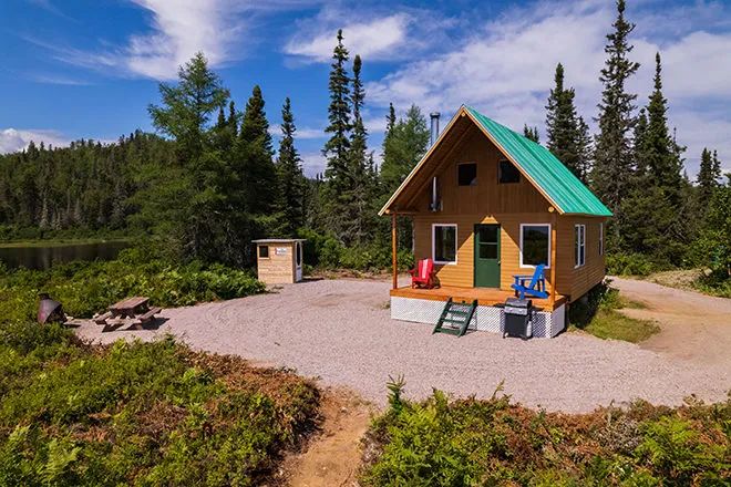 Vue extérieure du chalet numéro 3 avec sa galerie et son aire de détente en forêt.