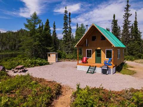 Vue extérieure du chalet numéro 3 avec sa galerie et son aire de détente en forêt.