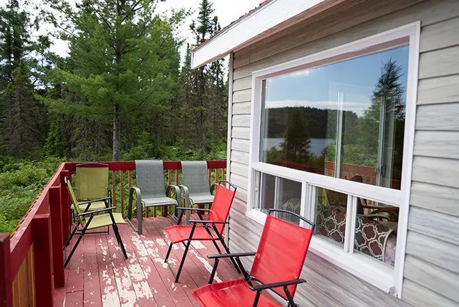 La galerie extérieure du chalet avec des chaises de jardin et une vue sur la forêt et le lac.
