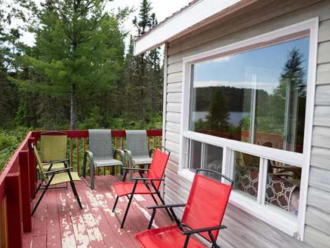 La galerie extérieure du chalet avec des chaises de jardin et une vue sur la forêt et le lac.
