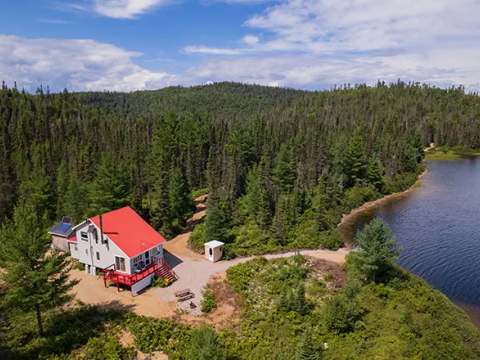 Vue aérienne du chalet au bord de l'eau entouré par la forêt.