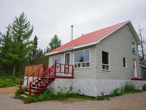 Le chalet numéro 5 avec son toit rouge et sa galerie en bois est situé en forêt.