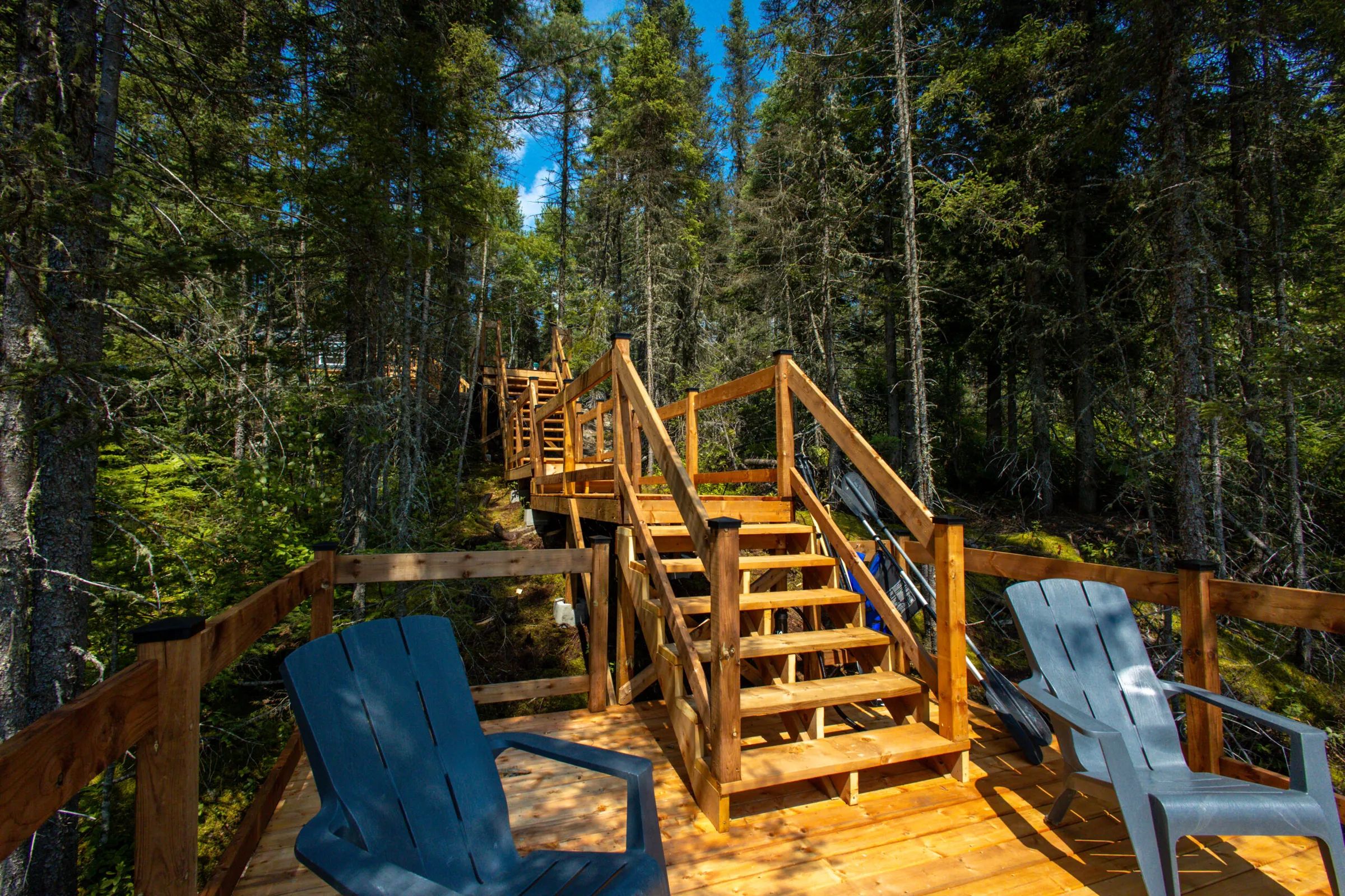 Un escalier en bois mène à un quai aménagé avec des chaises au bord de l'eau.