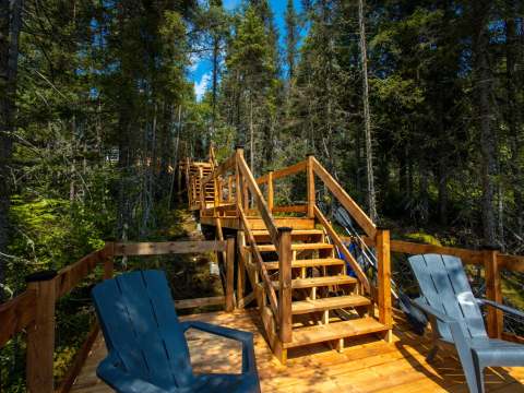 Un escalier en bois mène à un quai aménagé avec des chaises au bord de l'eau.