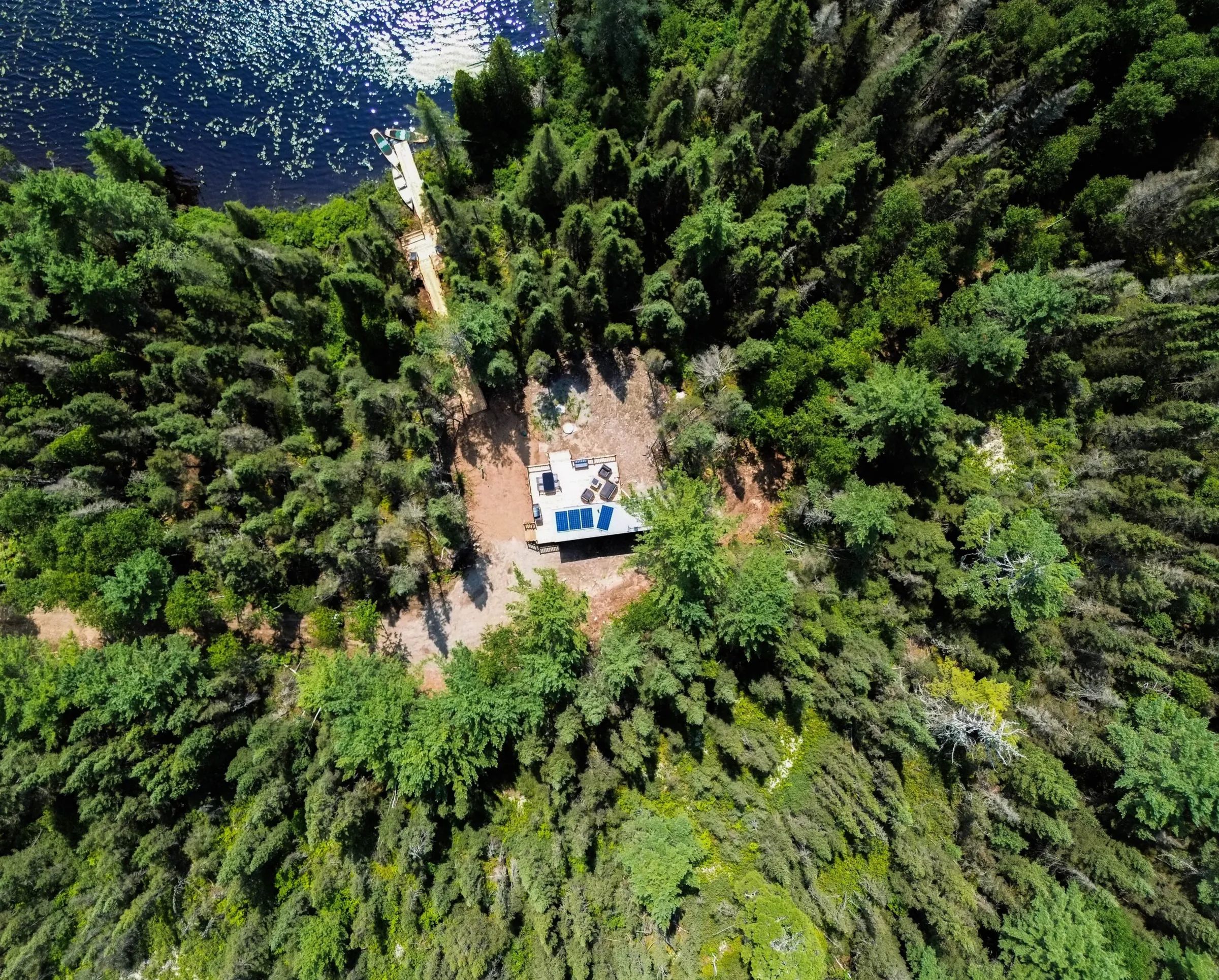Vue aérienne du chalet niché dans la forêt, avec son quai privé accessible par un sentier.