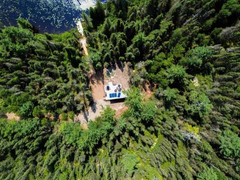 Vue aérienne du chalet niché dans la forêt, avec son quai privé accessible par un sentier.