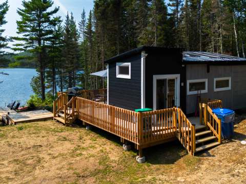 Overview of the tiny house with its large wooden deck by the water.
