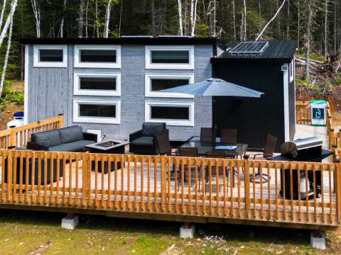 This tiny house features a large wooden deck with outdoor lounge, dining table, and barbecue.
