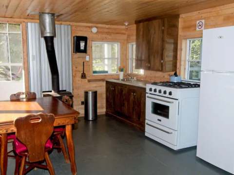 The equipped kitchen and dining area of cabin 6 with stove, refrigerator and wooden table.