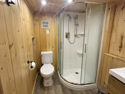 This private bathroom includes a modern shower and a toilet in a wooden decor.