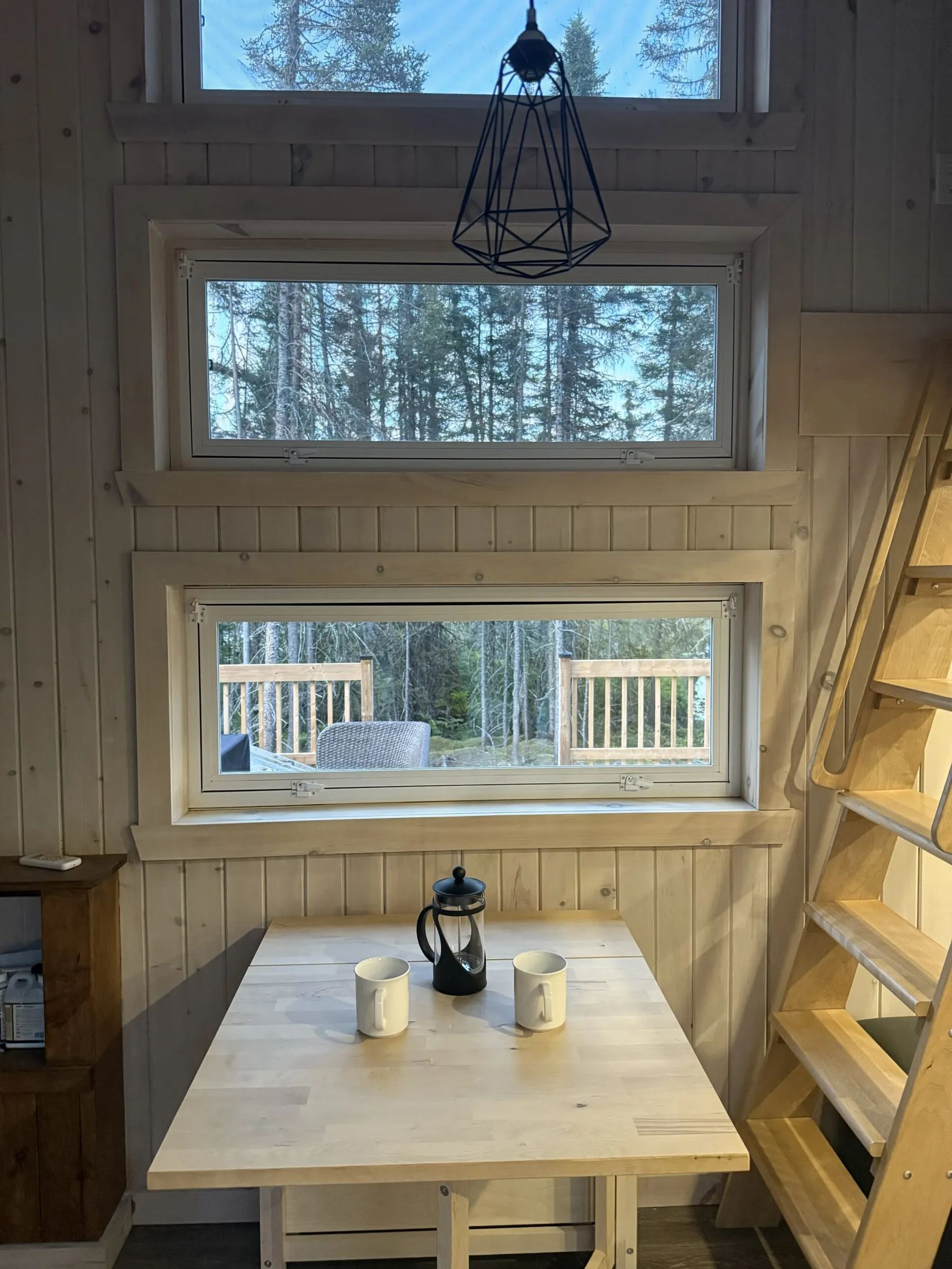 A wooden table with cups and a coffee maker in front of a window at cottage 8.