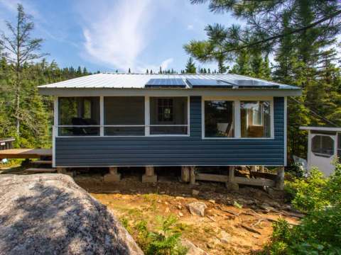 Façade du Chalet 1 entouré de forêt avec sa galerie grillagée et ses panneaux solaires sur le toit.
