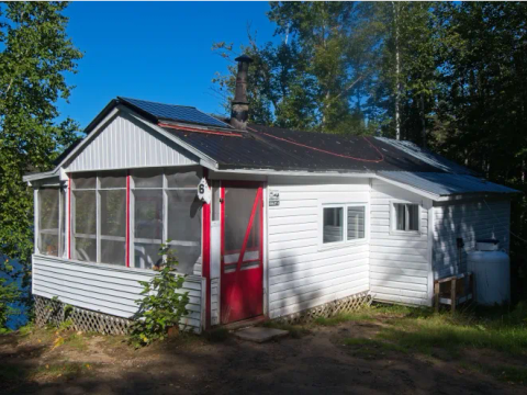 Vue extérieure du chalet 1 avec sa véranda grillagée et son environnement boisé.