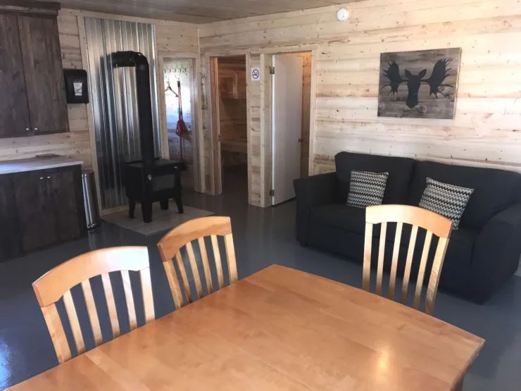 L'aire ouverte du chalet comprend une table à manger, un poêle à bois et un coin salon.