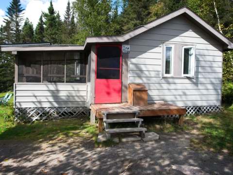 Vue extérieure du chalet comprenant une porte rouge, une petite galerie et une véranda grillagée.