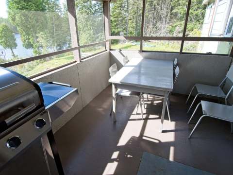 La véranda moustiquaire du chalet comprend un espace de repas et un barbecue avec vue sur le lac.