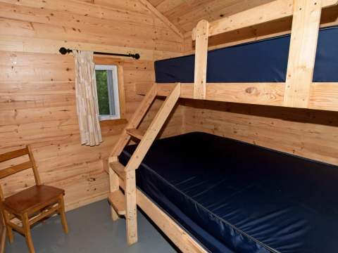 Cette chambre de chalet est équipée d'un lit superposé en bois et d'une chaise simple.