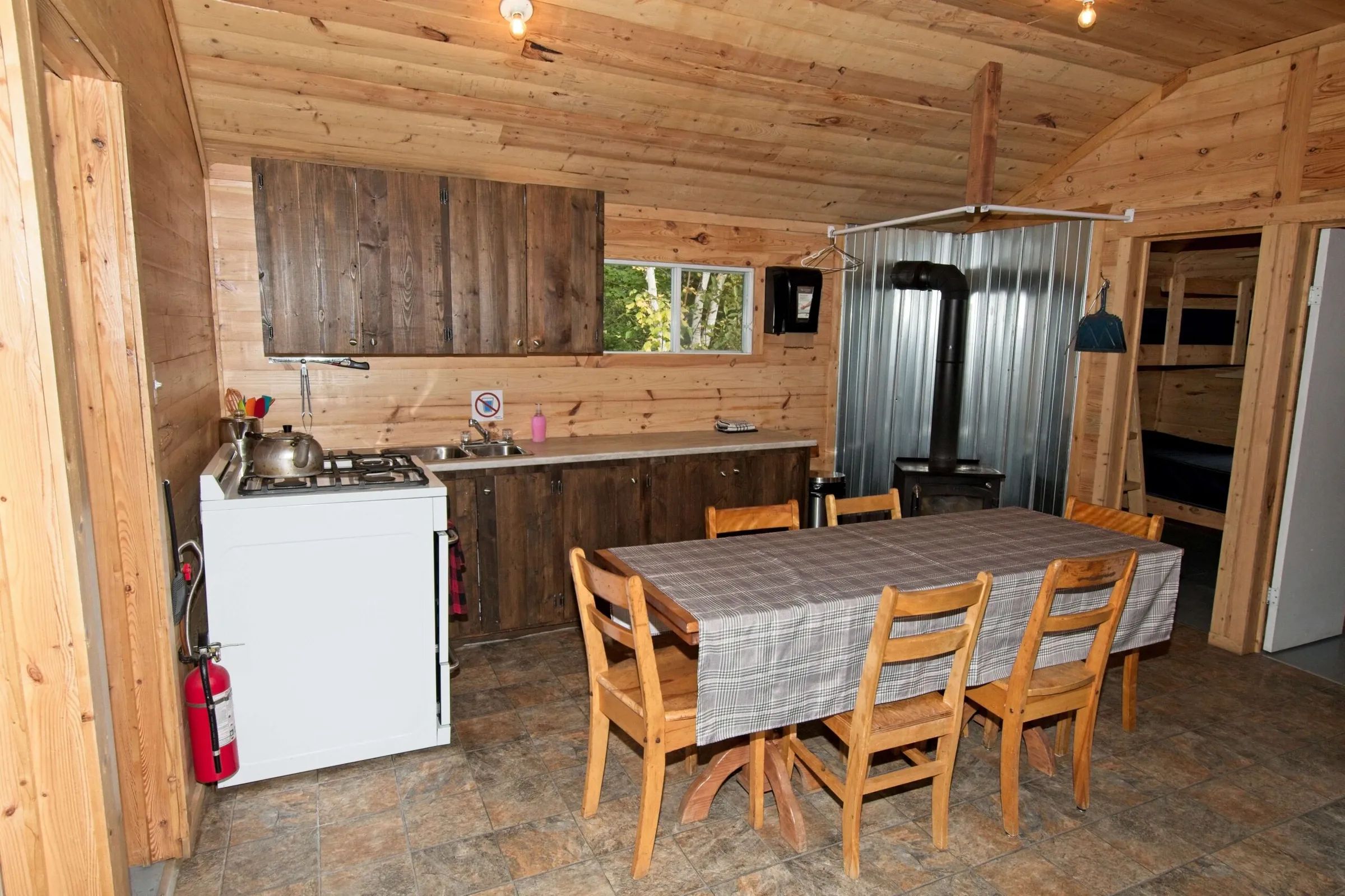 La cuisine et la salle à manger du chalet 4 incluent une cuisinière, une table et un poêle à bois.