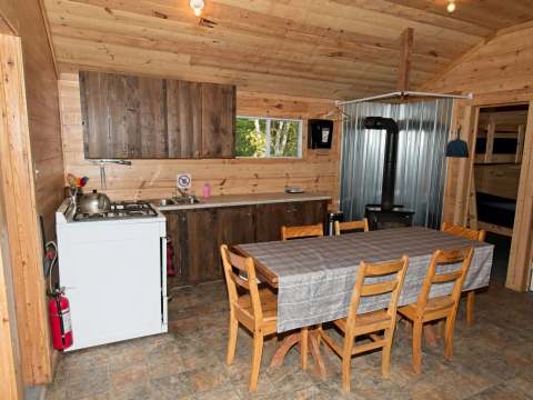 La cuisine et la salle à manger du chalet 4 incluent une cuisinière, une table et un poêle à bois.