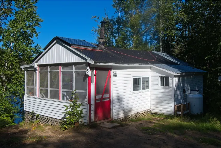 Vue extérieure du chalet 1 avec sa véranda grillagée et son environnement boisé.