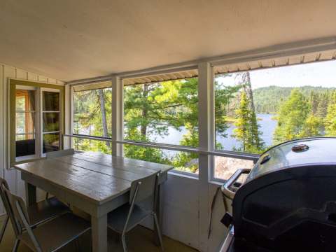 La véranda du chalet 5 offre une vue sur le lac et inclut une table à manger ainsi qu'un barbecue.