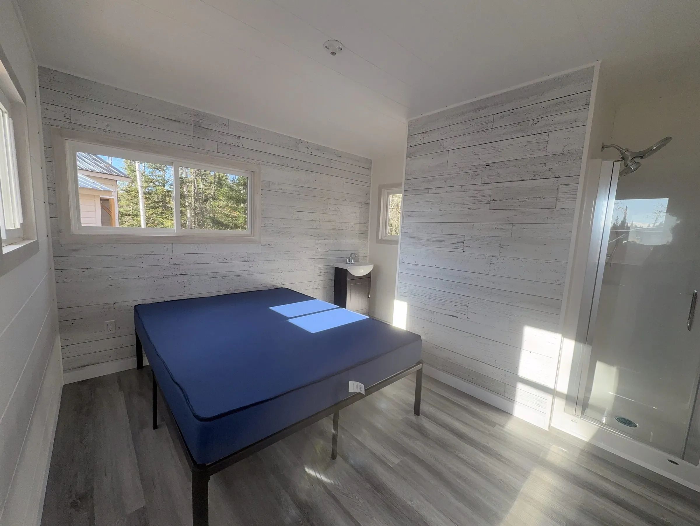 Vue intérieure de la chambre du chalet comprenant un lit, un lavabo et une douche intégrée.