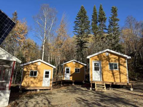 Vue extérieure des chalets de la pourvoirie situés en forêt sous un ciel bleu.