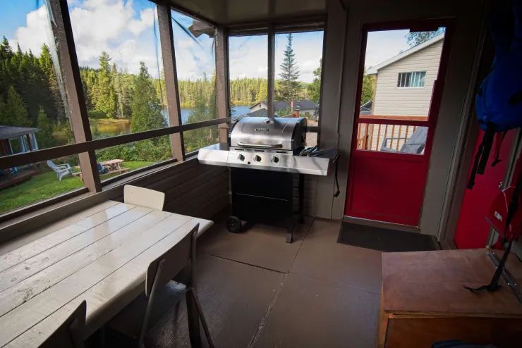 La véranda grillagée du chalet est équipée d'un barbecue et d'une table à manger avec vue sur le lac.