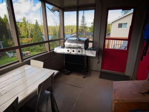 La véranda grillagée du chalet est équipée d'un barbecue et d'une table à manger avec vue sur le lac.