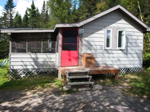 Vue extérieure du chalet comprenant une porte rouge, une petite galerie et une véranda grillagée.
