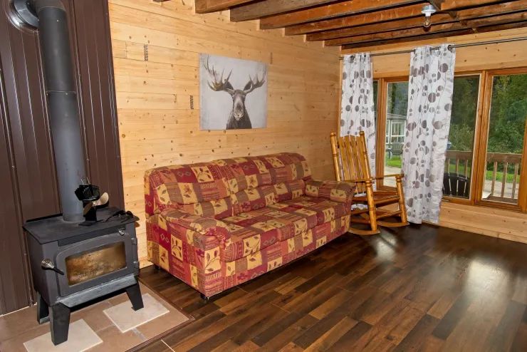 Le salon du chalet 3 comprend un foyer au bois, un canapé confortable et une chaise berçante.
