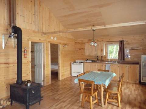 The open-concept cottage area includes a fully equipped kitchen, a dining table, and a wood stove.