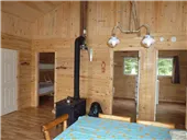 View of the cabin's living area with wood stove, dining table, and access to the bedrooms.