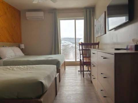 This inn room features two beds, a television, and a patio door looking out to the exterior.