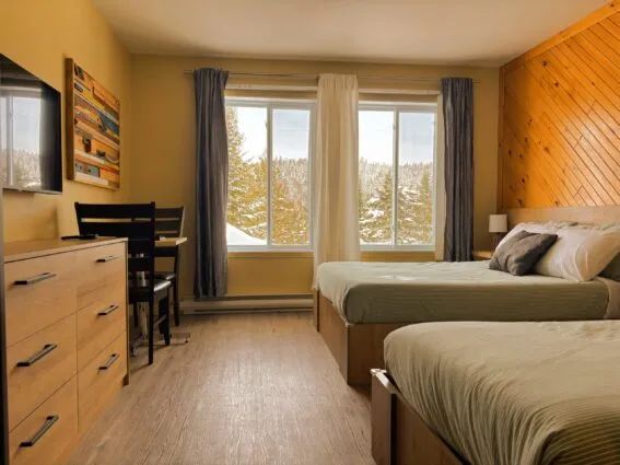 A bright inn room equipped with two beds and a workspace.
