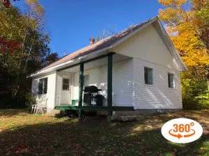 The La Loutre cabin is surrounded by trees in the forest with a covered porch and a barbecue.