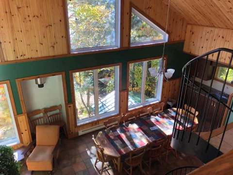 The cottage's dining area features a large wooden table with views of the surrounding forest.
