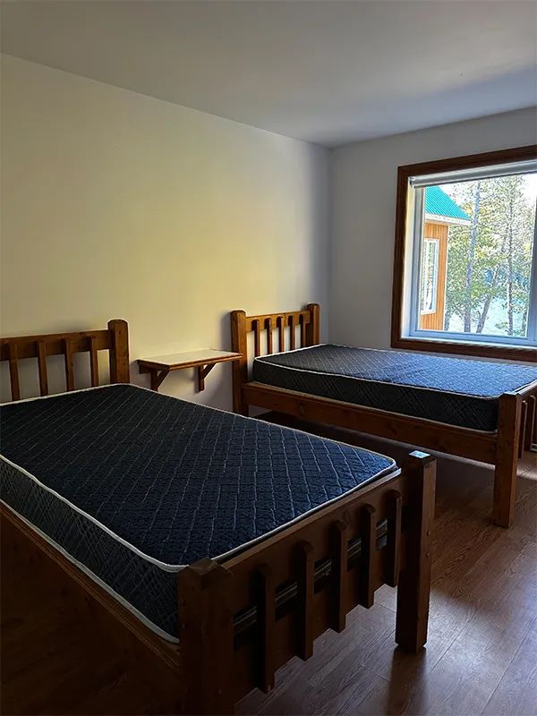 This chalet bedroom features two single beds with a view of the forest and the outdoors.