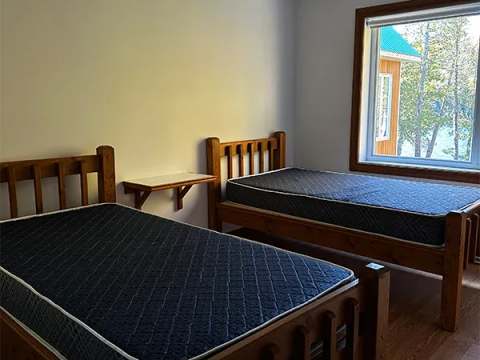 This chalet bedroom features two single beds with a view of the forest and the outdoors.