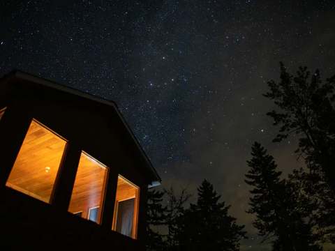 The cottage is illuminated under a starry sky at night.