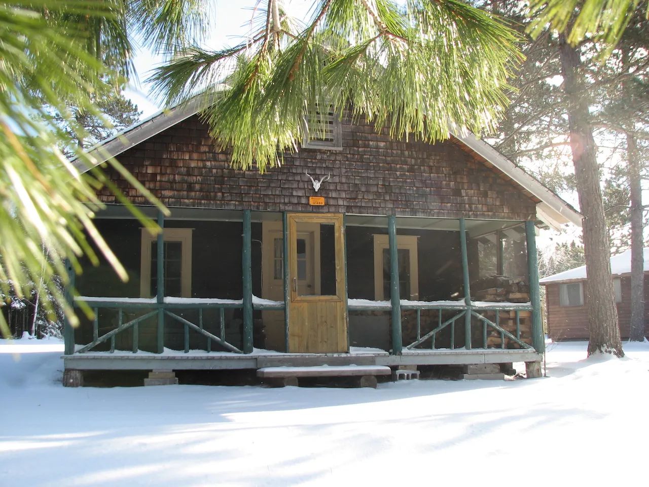 Façade d'un chalet en bois rond avec une galerie couverte sous une fine couche de neige.