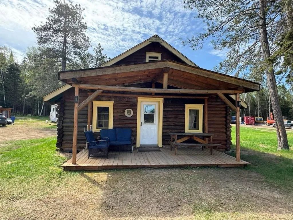 Vue de face du chalet en bois rond avec sa galerie couverte et son mobilier extérieur.