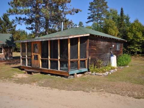 Exterior view of the log cabin with its screened porch in a forest setting.