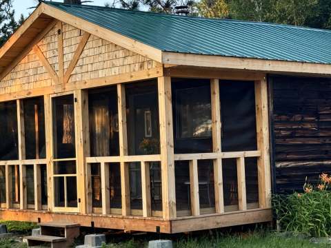 Side view of the L'Aigle cabin featuring its screened porch and green metal roof.