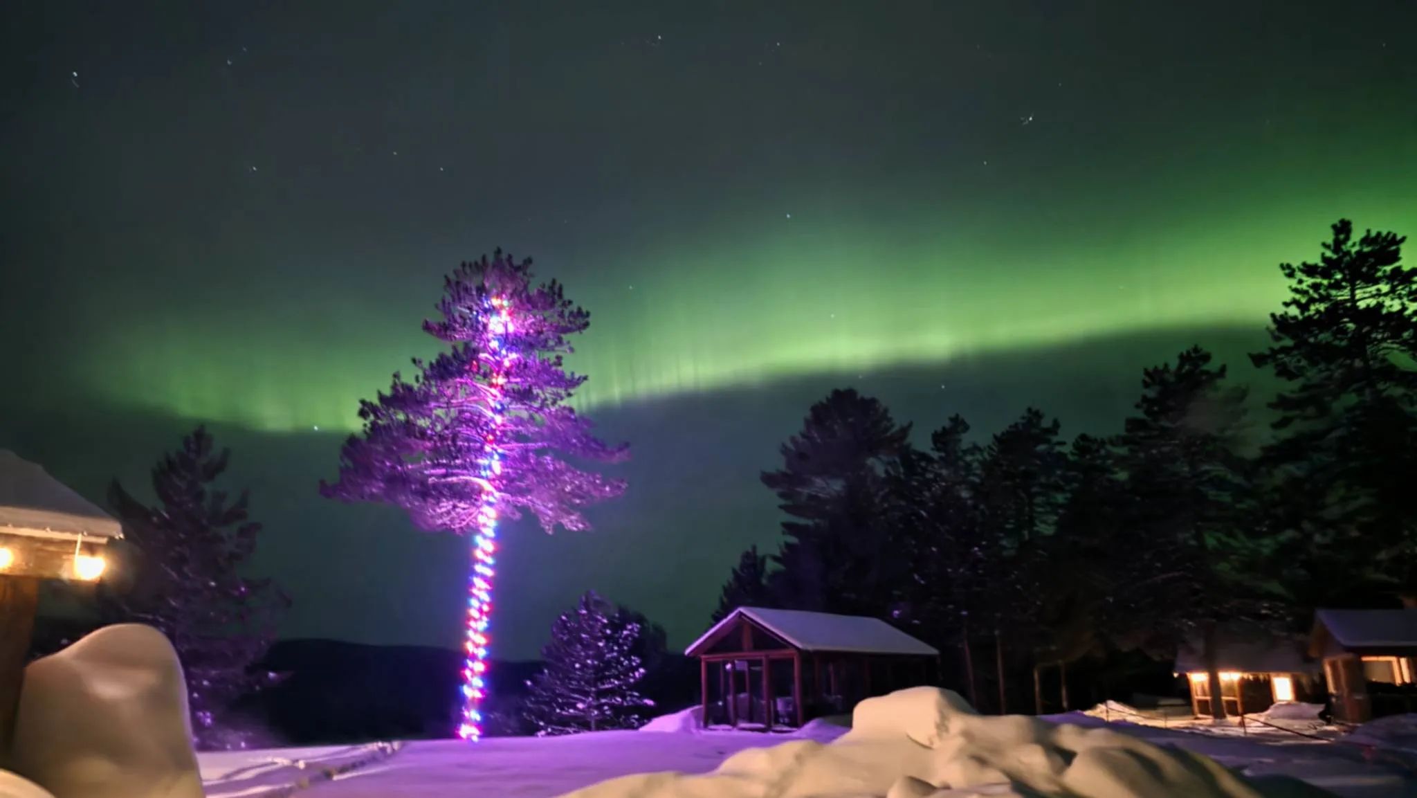 Vue nocturne du chalet sous les aurores boréales en hiver.
