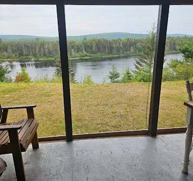 Vue imprenable sur la rivière et la forêt depuis la galerie couverte du chalet.