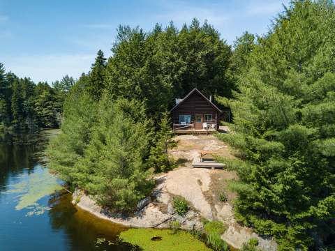 Aerial view of our rustic log cabin located by the lake and surrounded by trees.