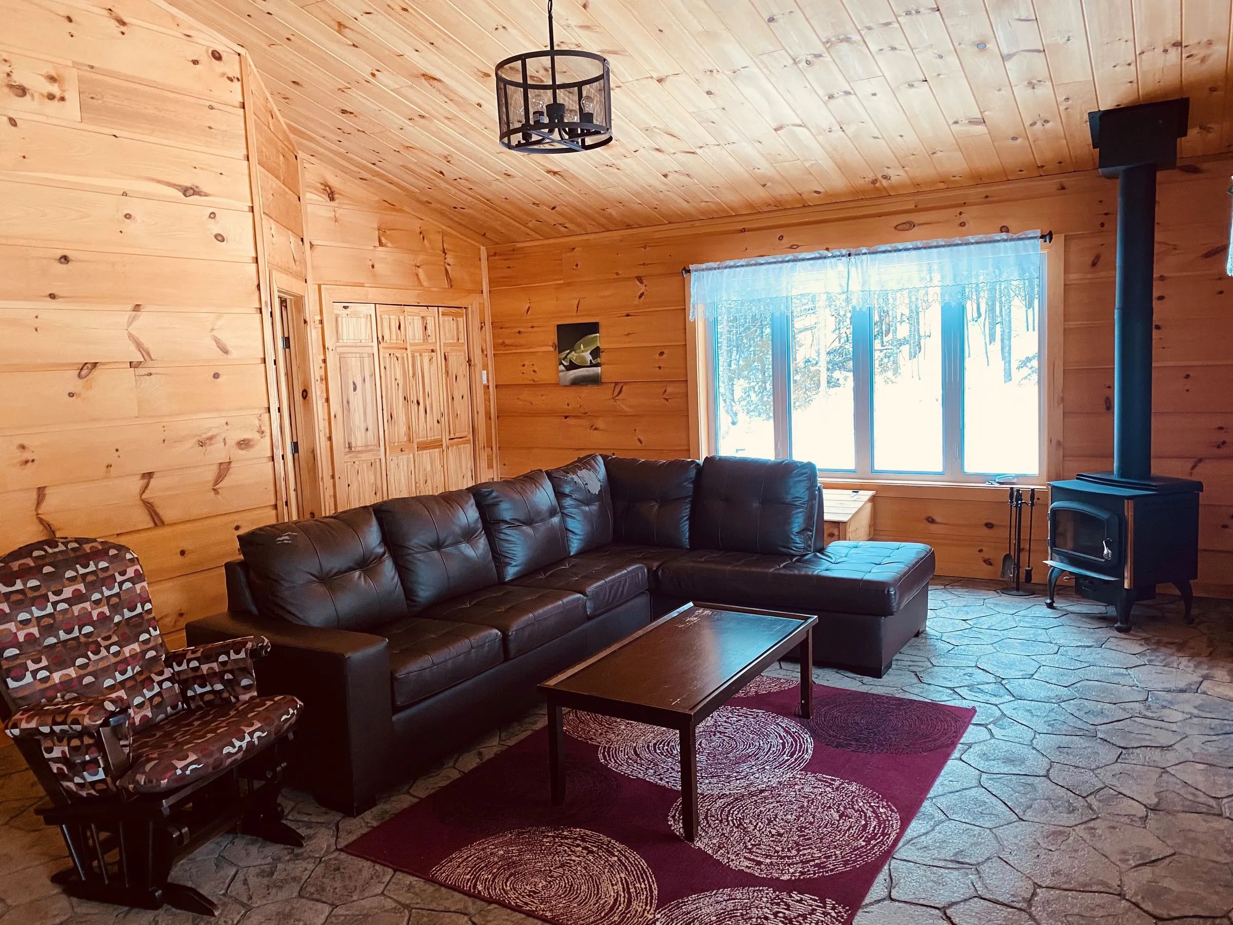 The chalet living room features a comfortable sofa, a chair, and a wood stove.